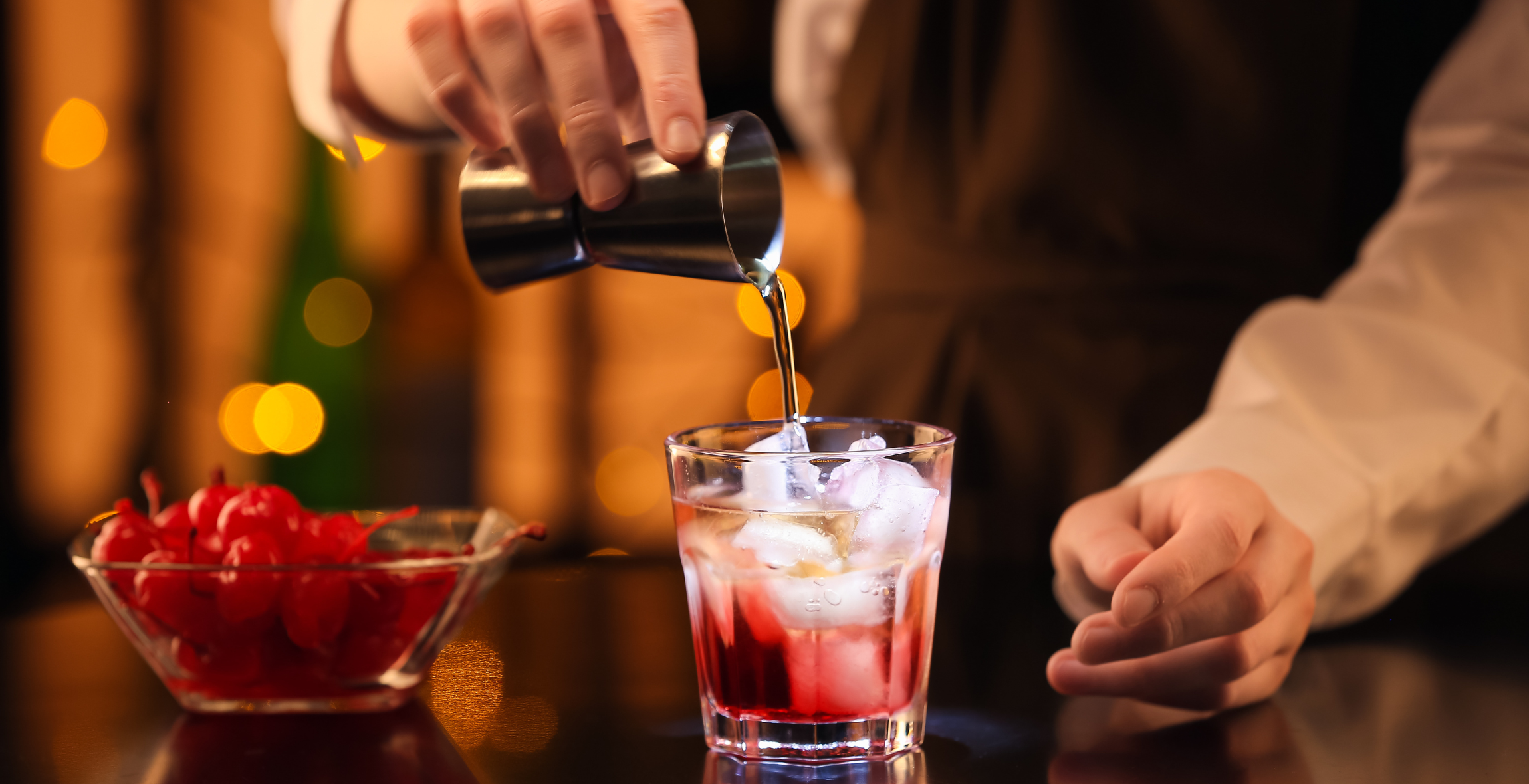 Bartender pours a shot into a glass with ice to make a drink at a bar.