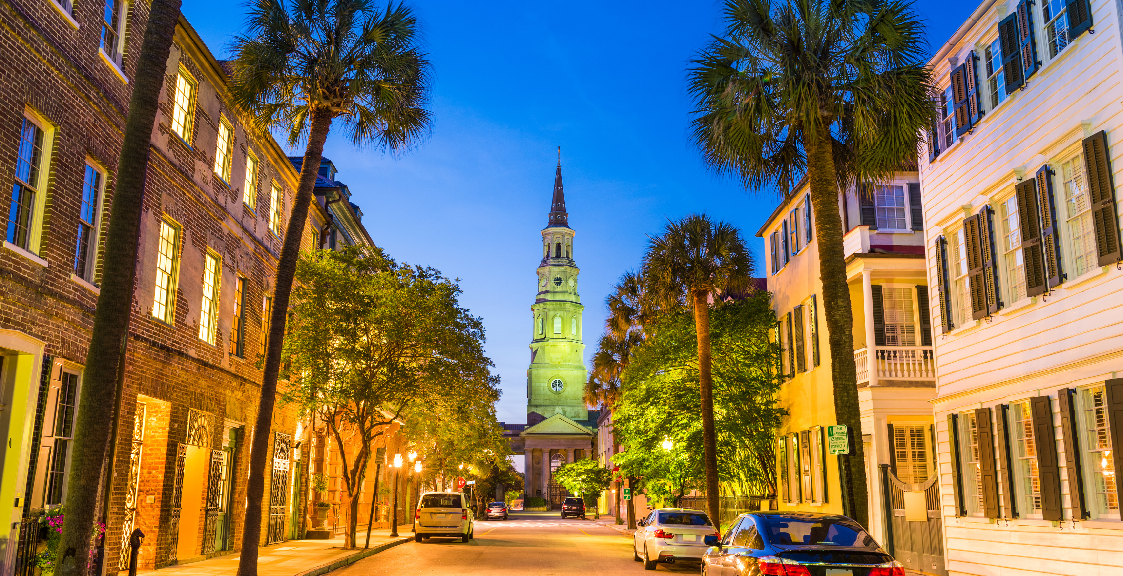 palm trees, houses and apartments lead to a hisoric white steeped church in Charleston, South Carolina